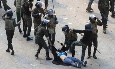 Photograph: a crowd of helmeted riot police surround and strike a man on the ground.