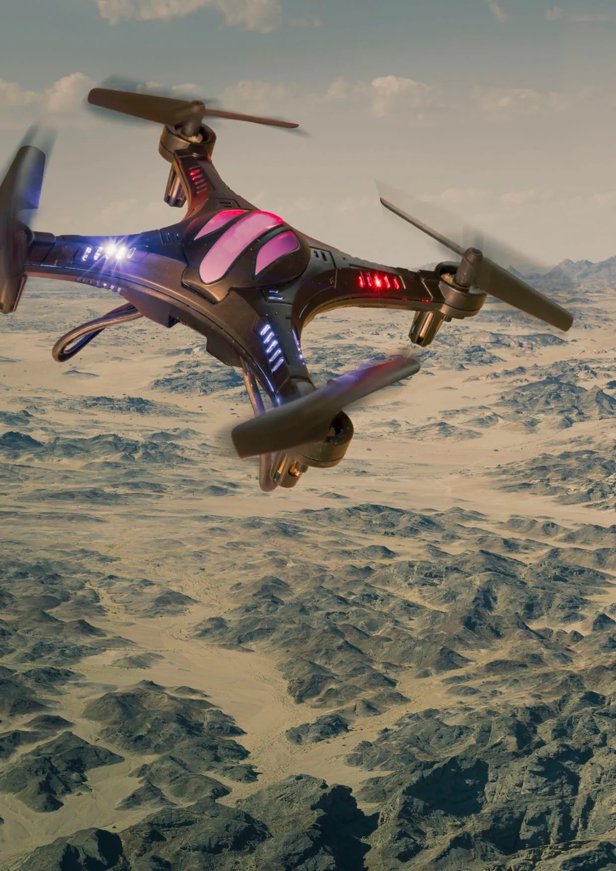 A quadcopter drone with coloured lights flies over a desert landscape.